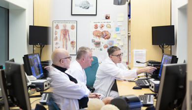 Foto av tre menn som sitter sammen på et kontor og ser på en skjerm