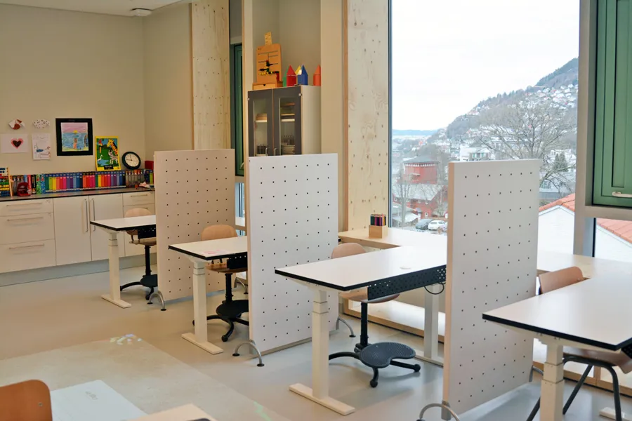 Klasserom med pulter og stoler på rekke langs viduene.