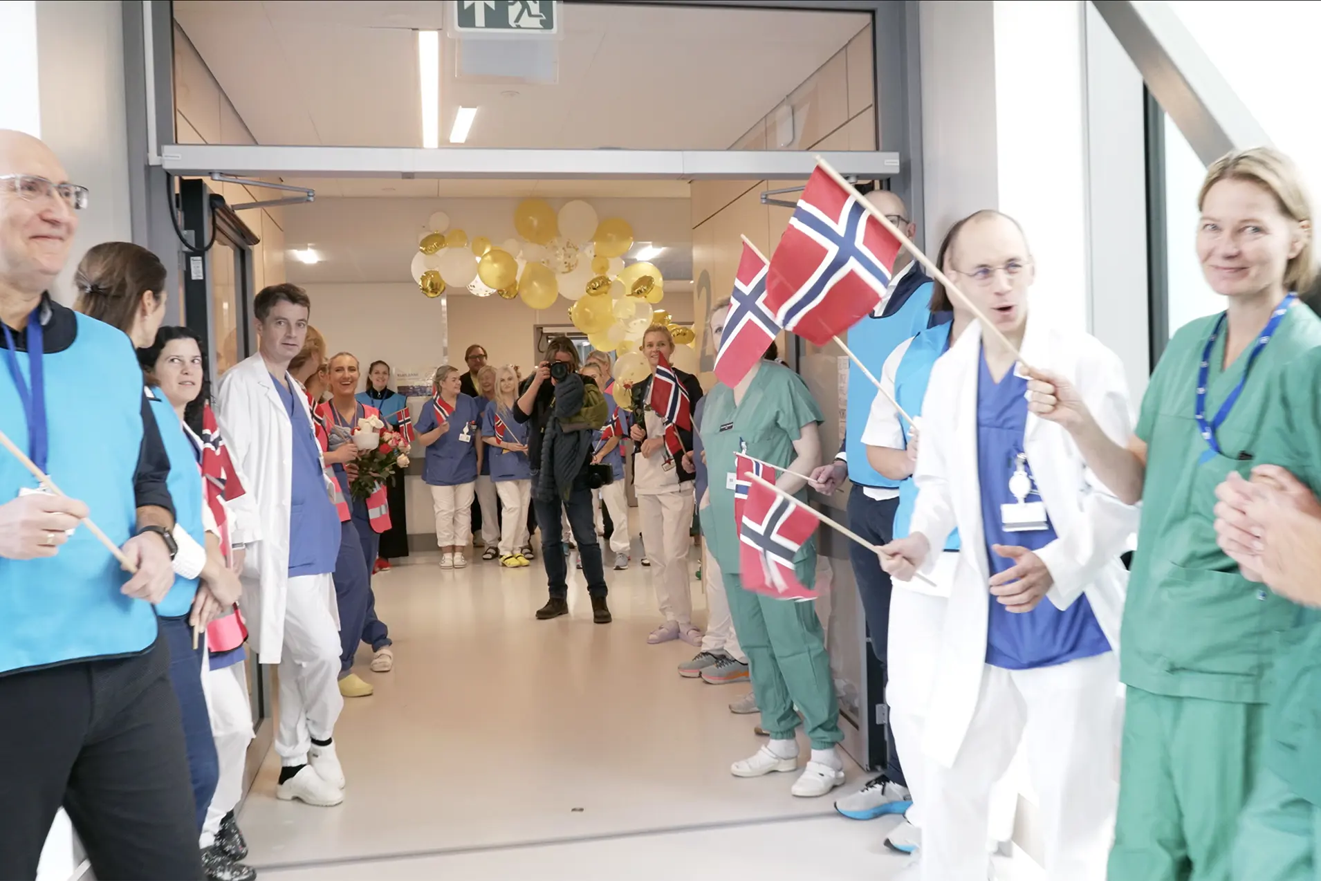 Ei gruppe menneske, helsepersonell, tilsette, pasientar og pårørande oppstilte med flagg, ballongar og tog.