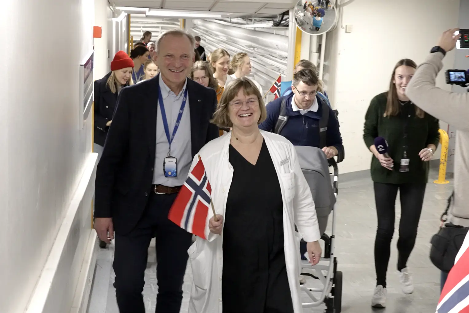 Ei gruppe menneske som går i tog i tunnel, med flagg og folk som filmar og tar bilde.