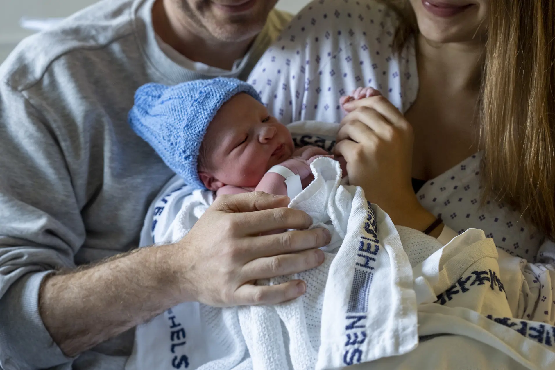 Far og mor som holder nyfødd baby med blå strikkelue.