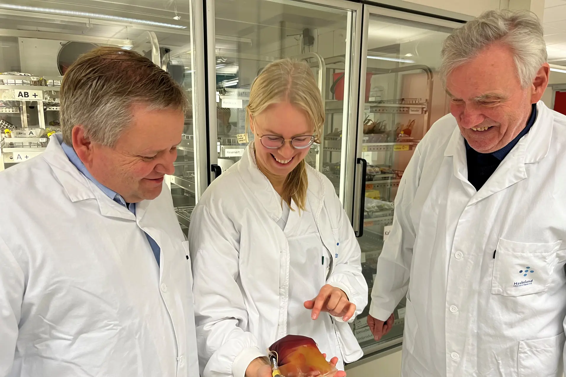 Tre mennesker i hvite frakker ser på en pose blodplasma