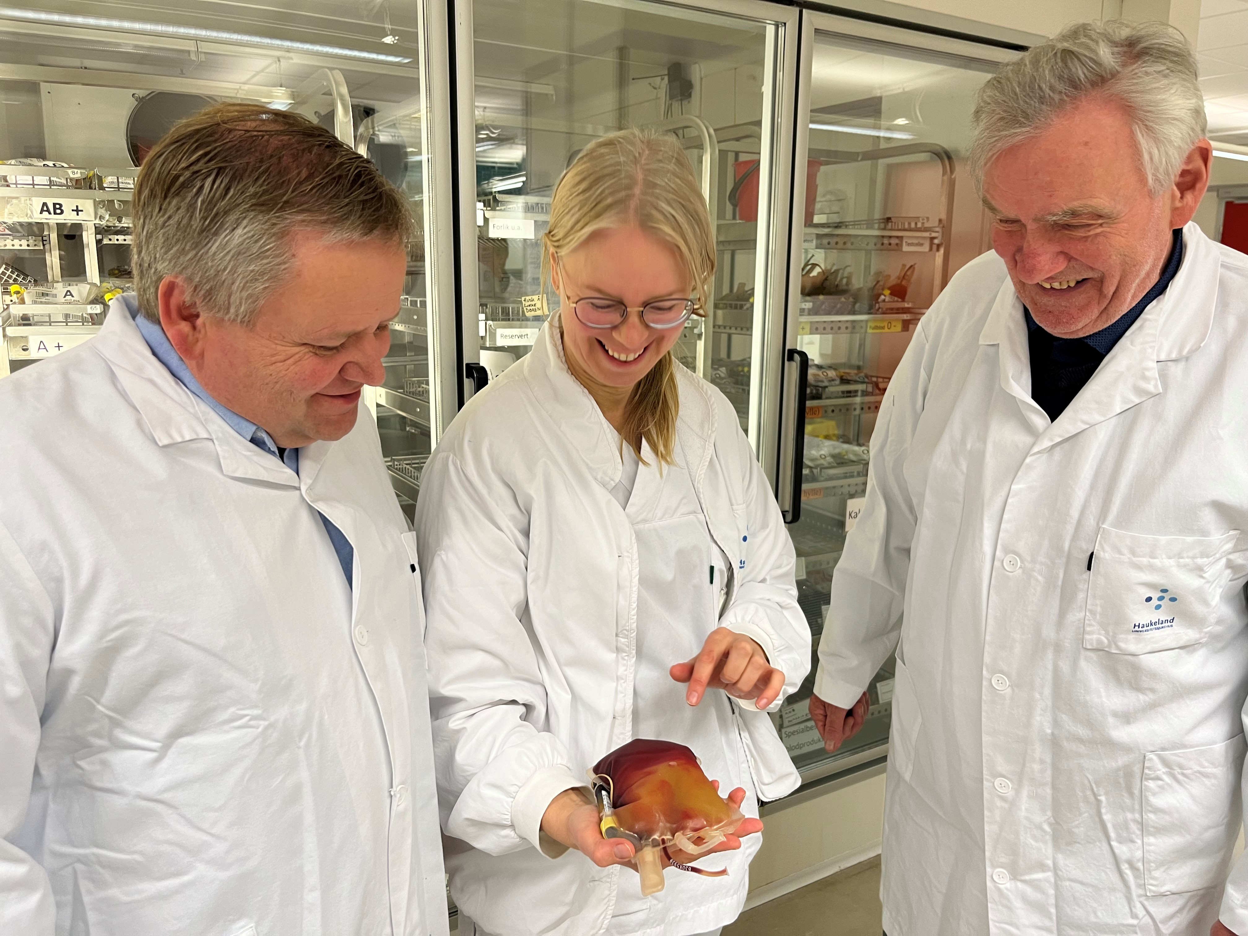 Tre mennesker i hvite frakker ser på en pose blodplasma