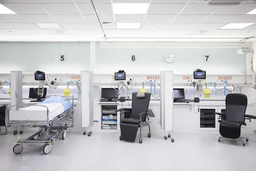 Viser et pasient rom hvor det står en oppredd, ren seng til venstre, en stol i midten og en stol til høyre. Med overvåkningsutstyr rundt alle enhetene
