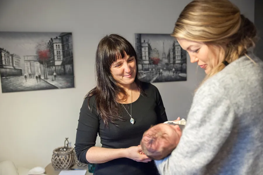 En kvinne ser på nyfødt barn i armene til moren.