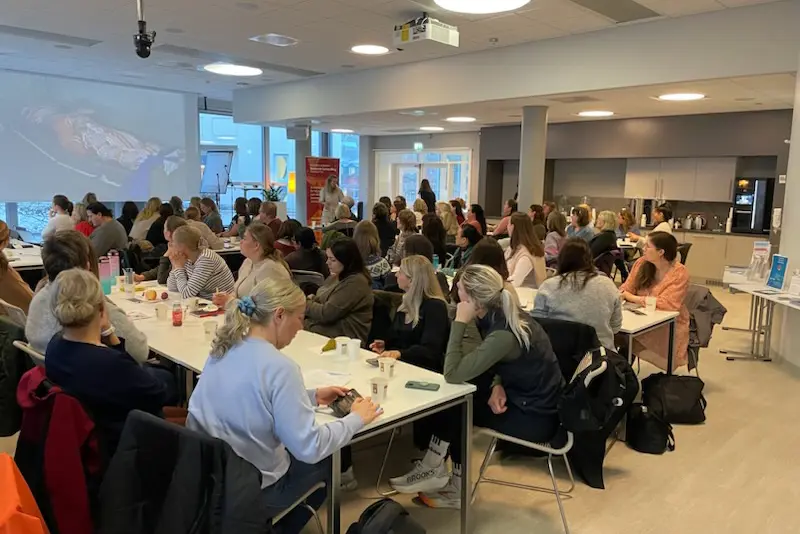 En gruppe mennesker som sitter ved bord i konferansesal