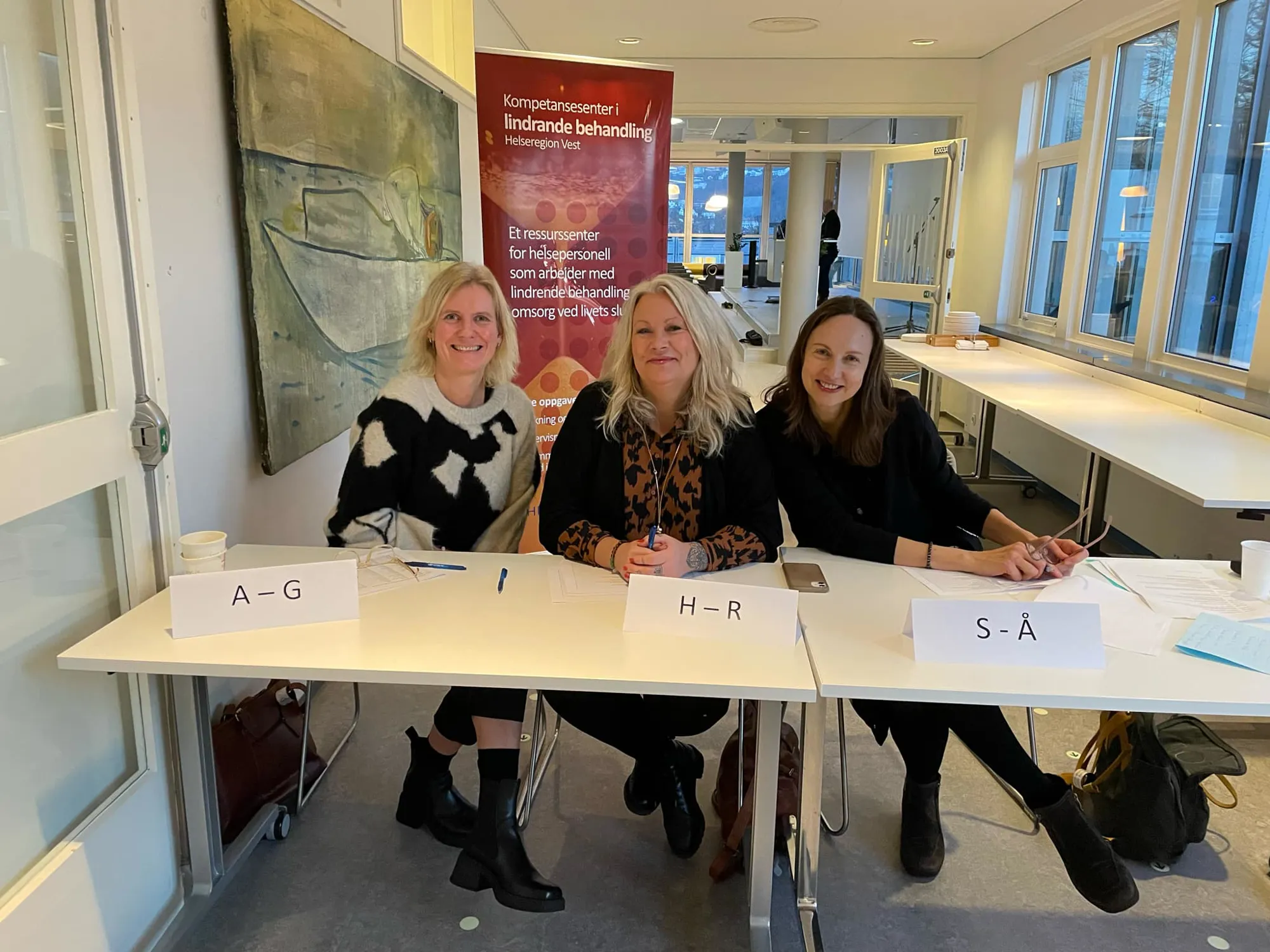 Tre kvinner som sitter ved et bord med skilt