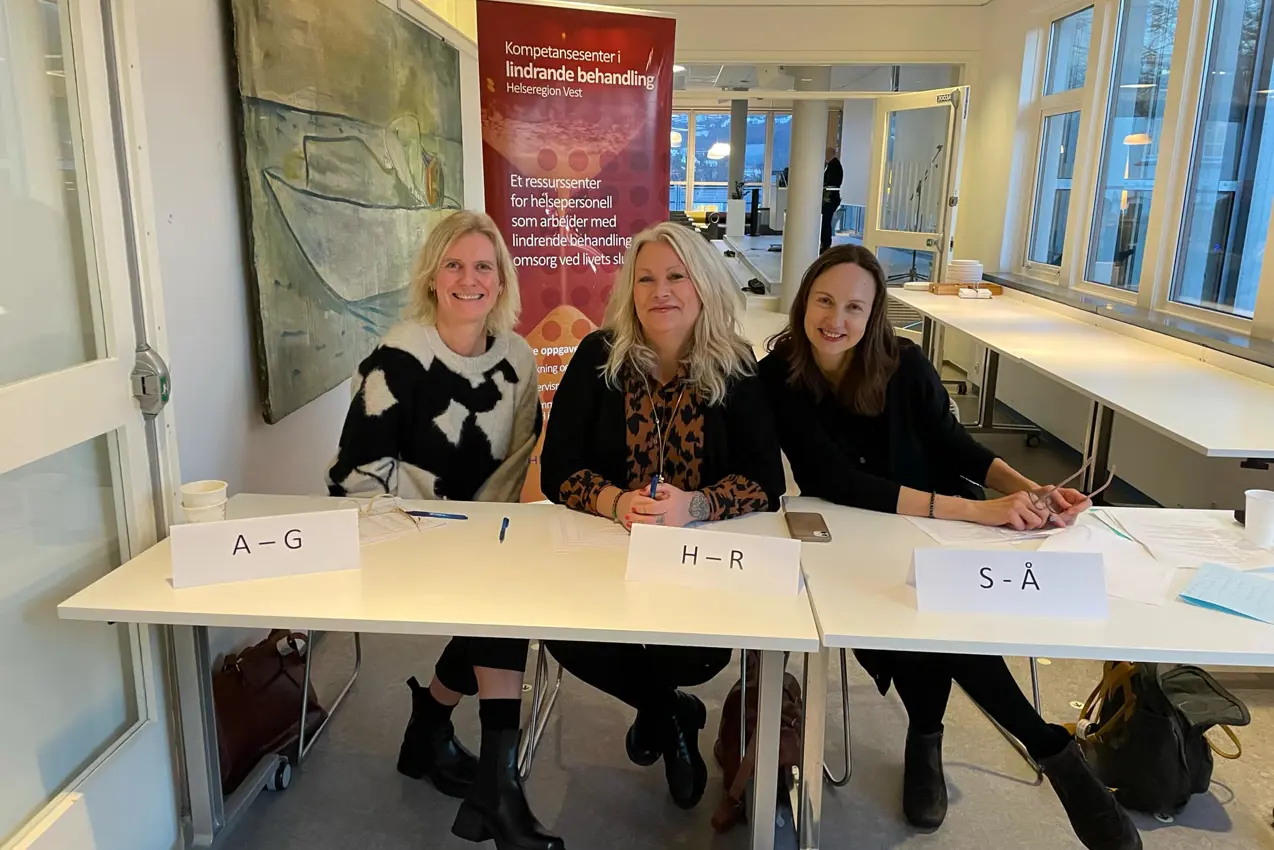 Tre kvinner som sitter ved et bord med skilt