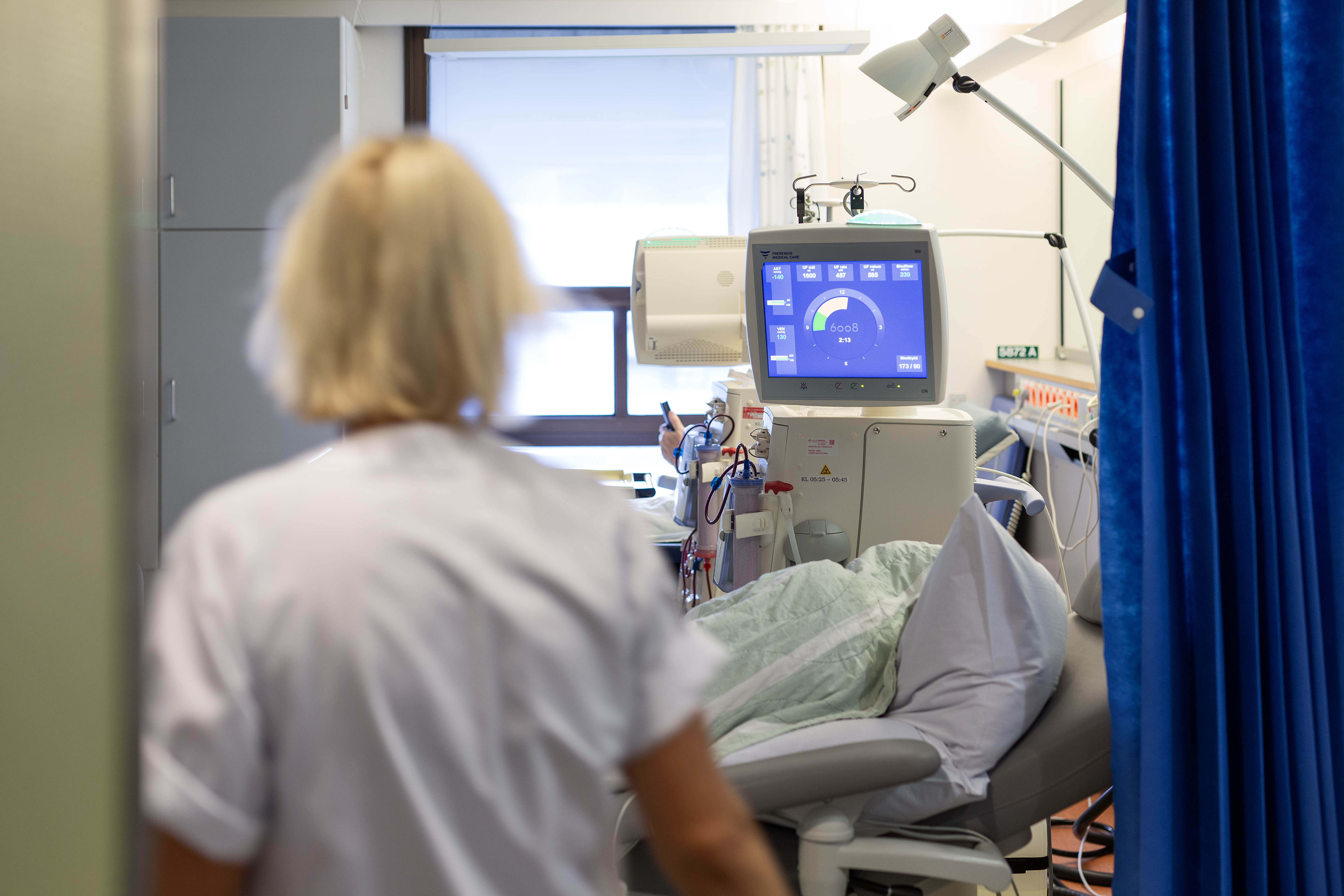 Sykepleier i hvit uniform med dialysemaskin og pasient