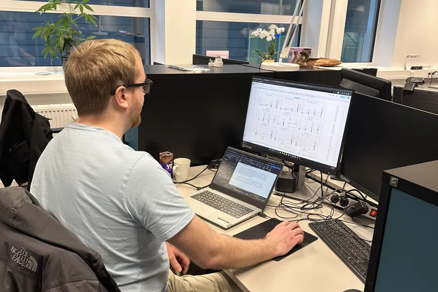 En mann som sitter ved et skrivebord med en bærbar datamaskin og en datamaskin