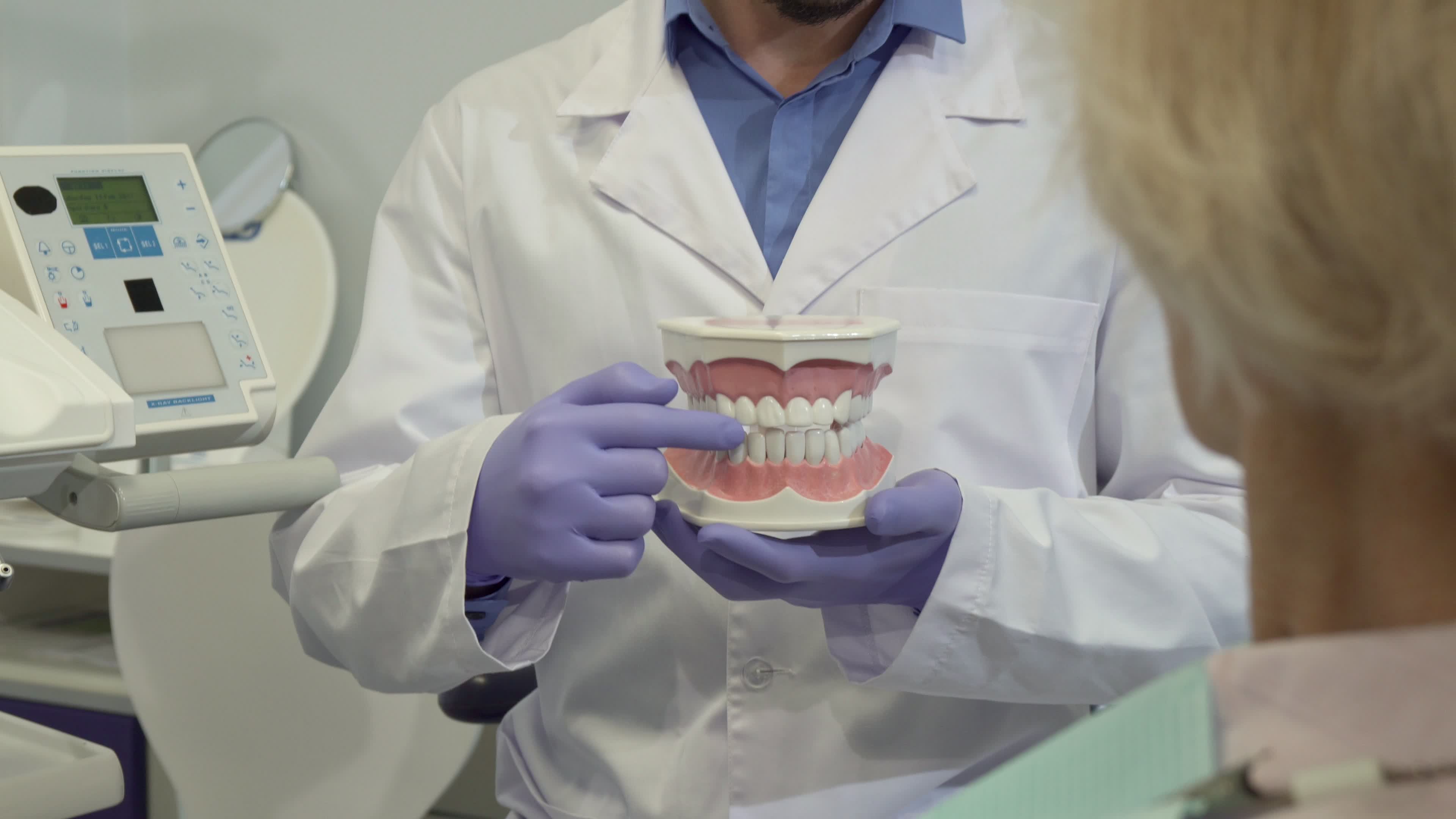 En person i hvit frakk som holder en tannmodell.