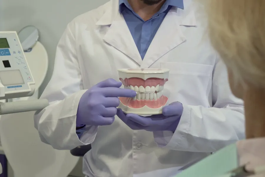 En person i hvit frakk som holder en tannmodell.