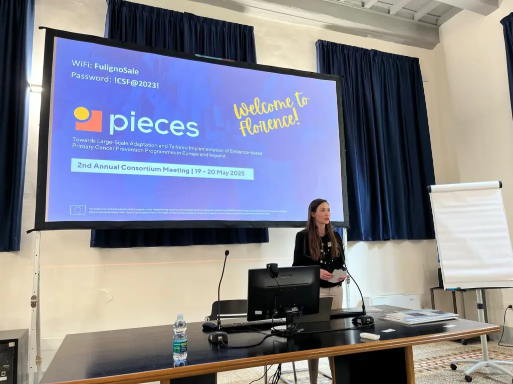 En person som står ved en talerstol foran en stor skjerm