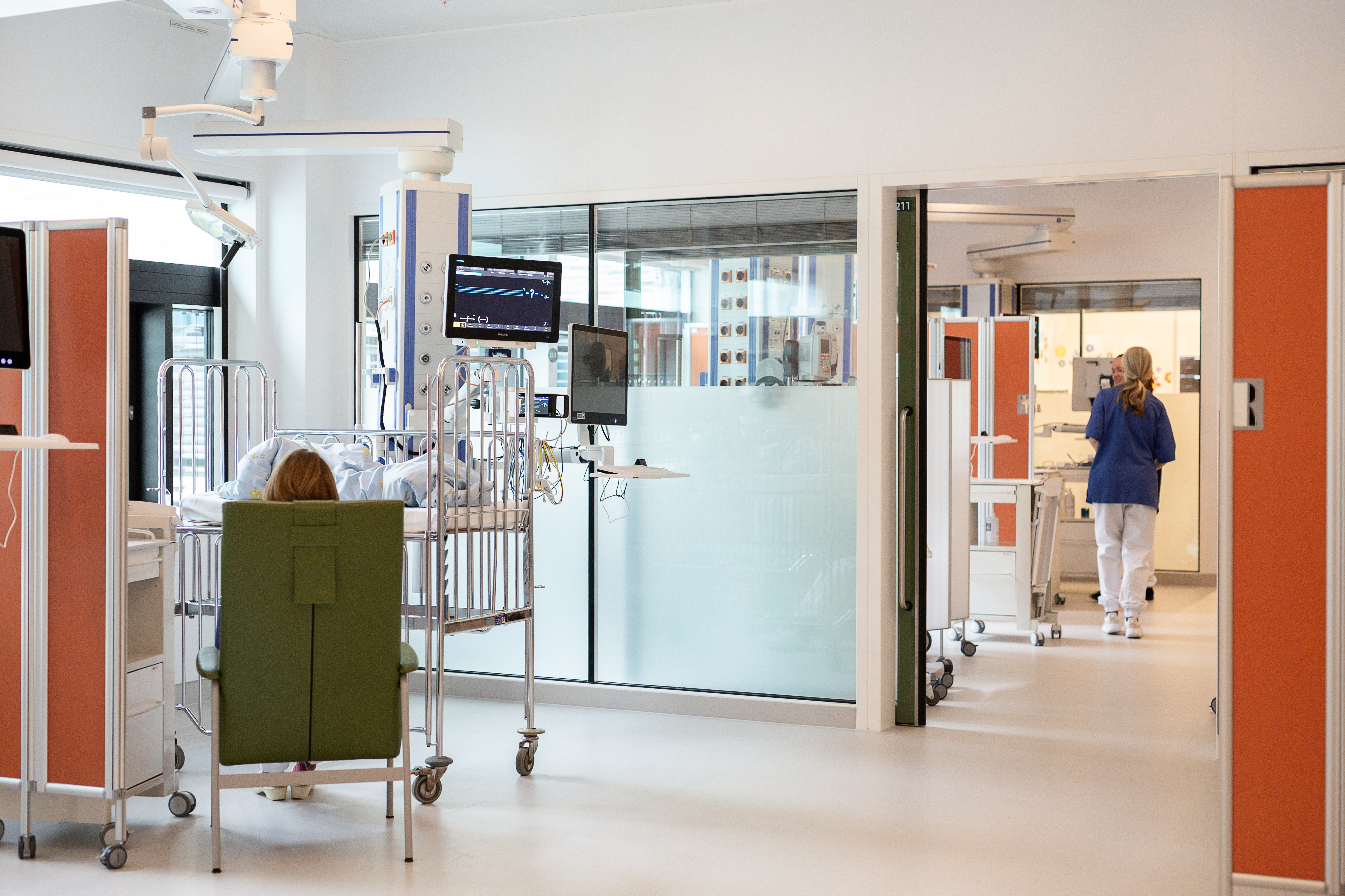 Et sykehusrom med en seng og en person som sitter i en stol