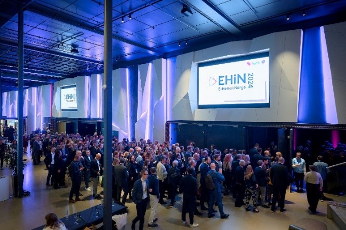 En gruppe mennesker som står i et rom med en stor skjerm