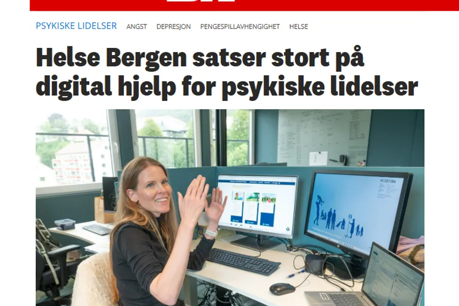 En person som sitter ved et skrivebord med en datamaskin og en bærbar PC