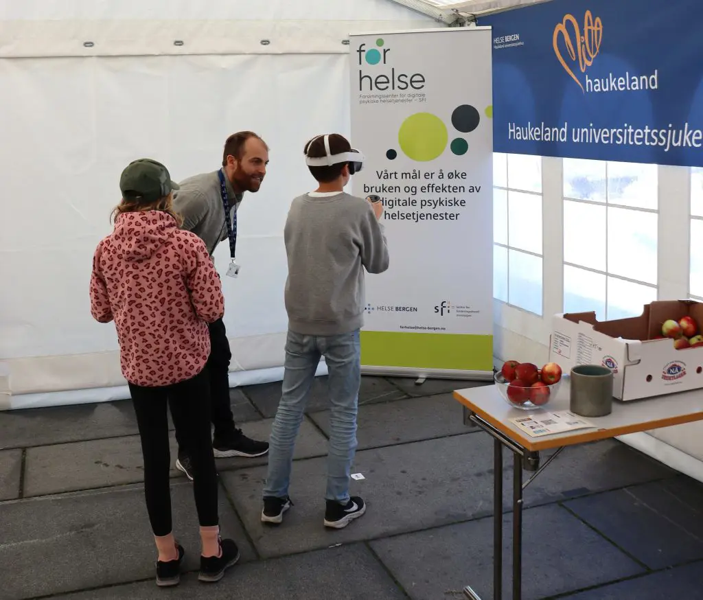 En gruppe mennesker som står i et rom med et bord og et skilt